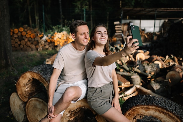 Foto junges paar sitzt auf gefällten bäumen im wald und macht selfies auf ihren handys