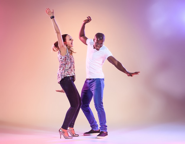 Foto junges paar tanzt soziale karibische salsa, studioaufnahme auf lila hintergrund. positive menschliche emotionen. die schwarzafrikanischen und kaukasischen models