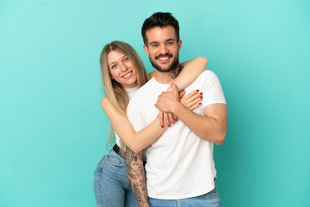 Junges Paar über isoliertem blauem Hintergrund lachen und umarmen