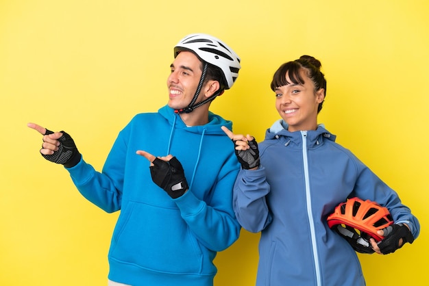 Junges Radfahrerpaar isoliert auf gelbem Hintergrund, das in seitlicher Position mit dem Finger zur Seite zeigt