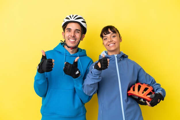 Junges Radfahrerpaar isoliert auf gelbem Hintergrund, das mit beiden Händen eine Daumen hoch Geste gibt und lächelt