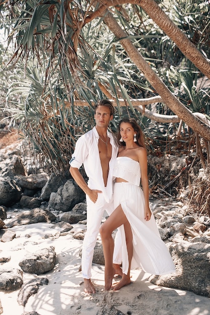 Foto junges romantisches paar in den weißen kleidern, die auf dem heißen tropischen strand umarmen und aufwerfen
