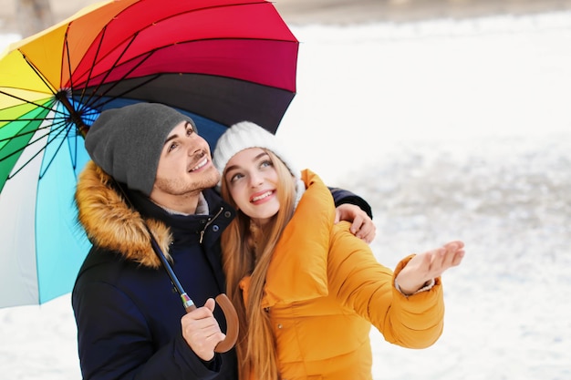 Junges romantisches Paar mit buntem Regenschirm am Wintertag