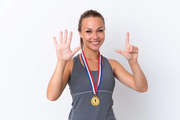 Junges russisches Sportmädchen mit Medaillen isoliert auf weißem Hintergrund, das sieben mit den Fingern zählt