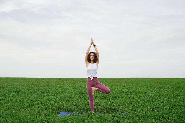 Junges schlankes Mädchen, das Yoga im Freien in einem grünen Feld tut