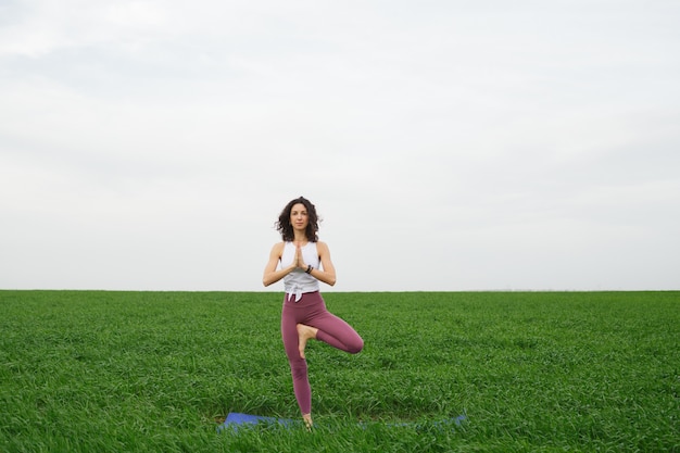 Junges schlankes Mädchen, das Yoga im Freien in einem grünen Feld tut