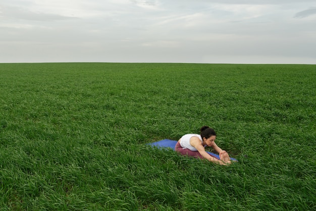 Junges schlankes Mädchen, das Yoga im Freien in einem grünen Feld tut