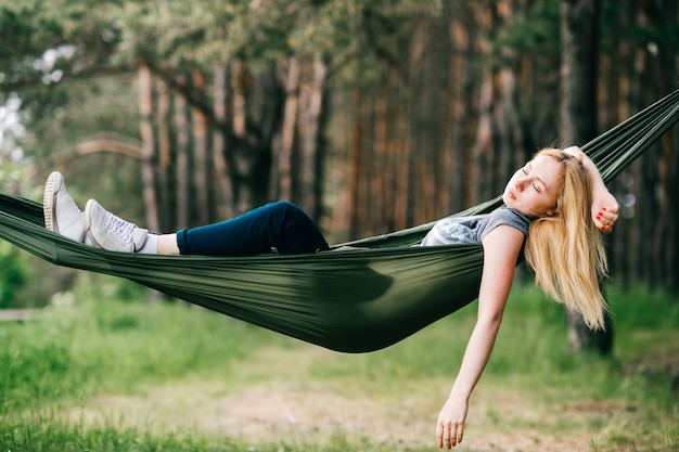 Junges schönes blondes Mädchen, das in der Hängematte an der Natur entspannt