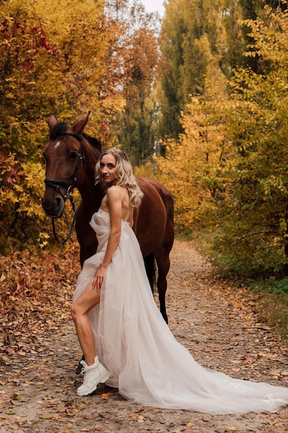 Junges schönes blondes Mädchen, das in einem Herbstpark mit einem Pferd aufwirft