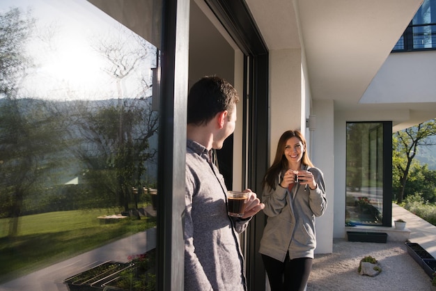 junges schönes hübsches paar, das morgens kaffee an der tür ihrer luxusvilla genießt