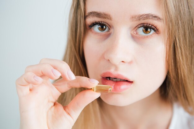 Junges schönes krankes Mädchen steckt eine Pille in den Mund. Mehrfarbige Kapseln, Tabletten, Vitamine, Nahrungsergänzungsmittel. Gesicht aus nächster Nähe. Tonen.