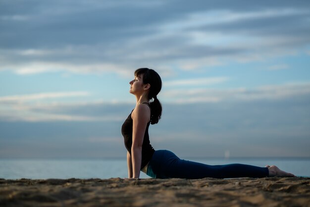 Junges schönes Mädchen an der Küste praktiziert Yoga