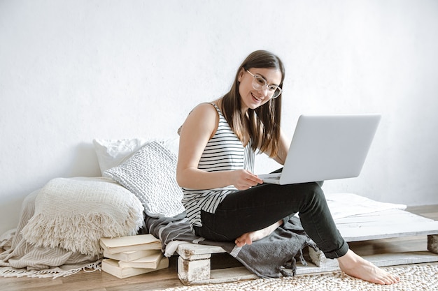 Junges schönes Mädchen arbeitet fern hinter einem Laptop zu Hause. Das Konzept der freiberuflichen Tätigkeit und der Arbeit im Internet.