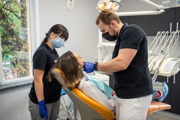 Junges schönes Mädchen beim Zahnarzt mit einem Assistenten erhält eine Behandlung mit Hilfe der neuesten Geräte der Zahnheilkunde