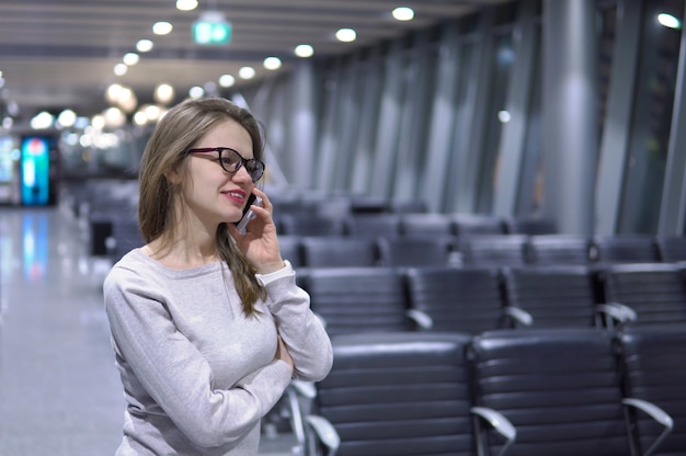 Junges, schönes Mädchen, das am Telefon in einem leeren Flughafenterminal spricht