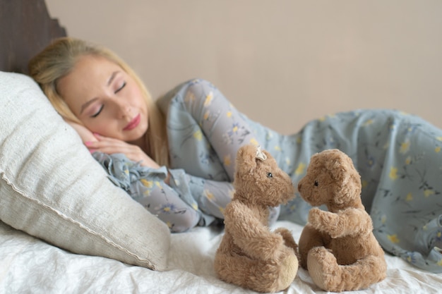 Junges schönes Mädchen, das auf Bett mit Kinderspielzeug wie Kind schläft.