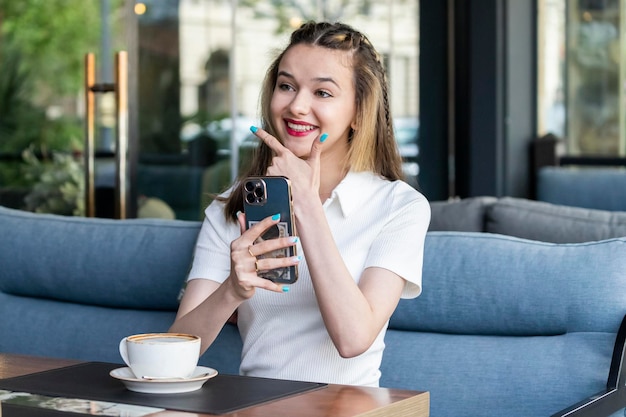 Junges schönes Mädchen, das ein Telefon hält und im Restaurant lacht