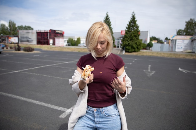 Junges schönes Mädchen, das Hotdog im Parkplatz isst.