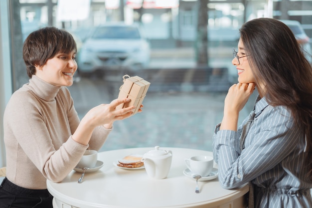 Junges schönes Mädchen, das mit ihrem Freund im Café sitzt und ein Geschenk erhält