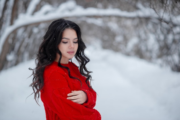 Junges schönes Mädchen, das roten Pullover im Winterpark trägt. Gesundes Lebens- und Schönheitskonzept. Mädchen, das Spaßkonzept hat. Horizontaler Copyspace