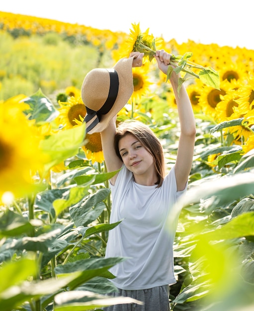 Junges schönes Mädchen geht im Sommer auf einem Feld mit blühenden Sonnenblumen