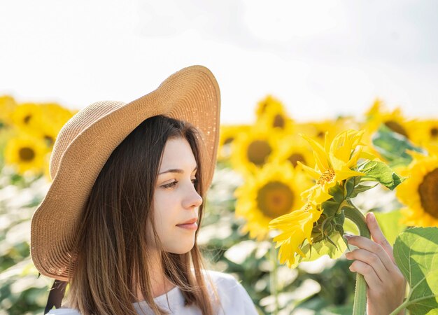 Junges schönes Mädchen geht im Sommer auf einem Feld mit blühenden Sonnenblumen