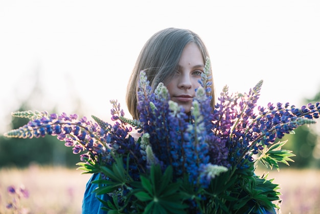 Junges schönes Mädchen hält einen großen Blumenstrauß von lila Lupinen in einem blühenden Feld. Blühende Lupinenblüten. umweltfreundlich. Naturkonzept. Weicher Fokus.