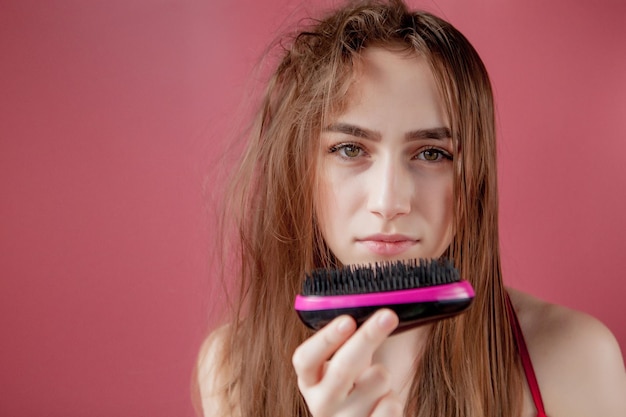 Foto junges schönes mädchen hat probleme, während haare auf rosa hintergrund