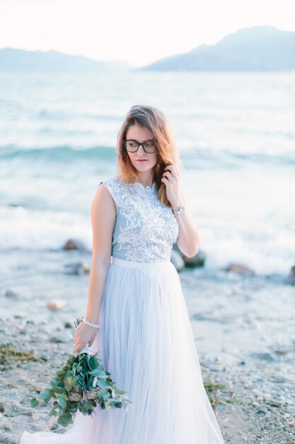 Junges schönes Mädchen in den Gläsern und im blauen Kleid, das nahe dem See geht. Lago di Garda in Sirmione. Italien