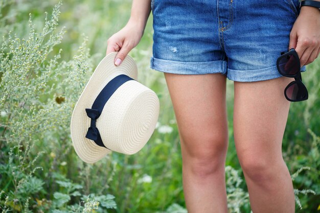 Junges schönes Mädchen in Denim-Overalls und einem leichten Hut, der im Park spazieren geht