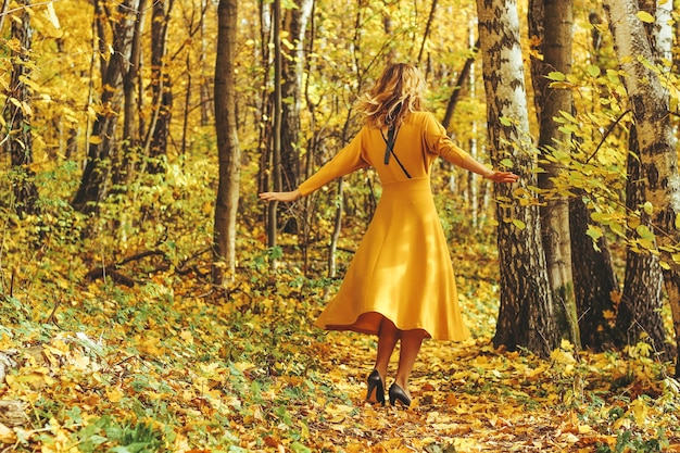 Junges schönes Mädchen in einem gelben langen Kleid geht im Herbstpark mit gefallenen Blättern