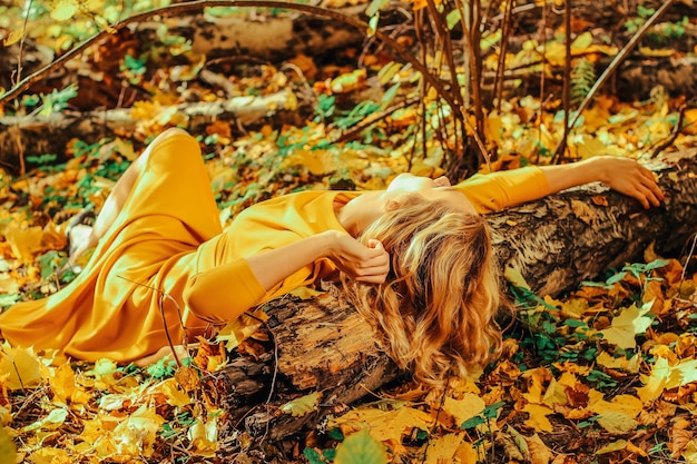 Junges schönes Mädchen in einem langen gelben Kleid, das auf dem Boden des Herbstparks liegt