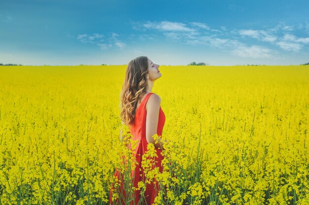 Junges schönes Mädchen in einem roten Kleid hautnah in der Mitte des gelben Feldes mit der Rettich-Blumen-Nahaufnahme.