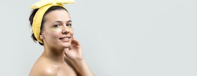 Junges schönes Mädchen in einem weißen Handtuch auf dem Kopf trägt Kollagen-Gel-Pflaster unter den Augen Maske unter dem Augenbehandlungsgesicht