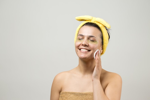 Junges schönes Mädchen in einem weißen Handtuch auf dem Kopf trägt Kollagen-Gel-Pflaster unter den Augen Maske unter dem Augenbehandlungsgesicht