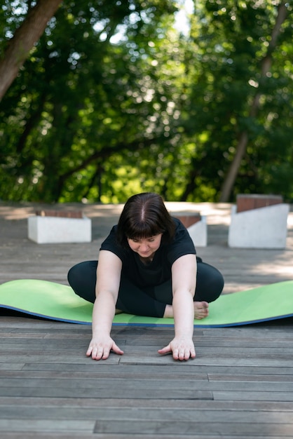 Junges schönes Mädchen lehnt sich aus einer sitzenden Position nach vorne. Trainer zeigt eine Lektion. Fitness im Park.