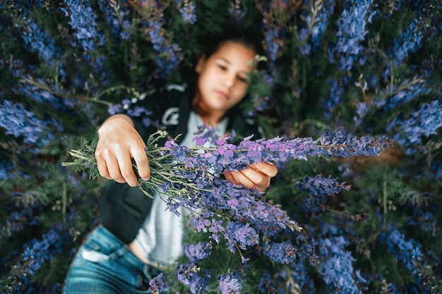 Junges schönes Mädchen liegt im Gras und hält einen Strauß lila Blumen in ihren Händen