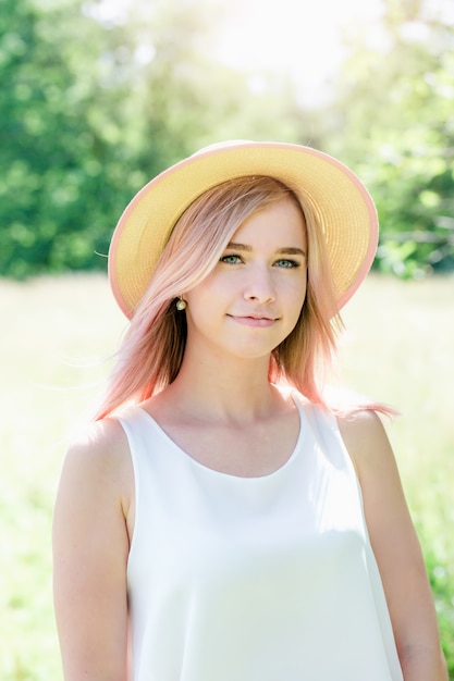 Junges schönes Mädchen mit rosa Haaren im Sommerhut auf der Lichtung