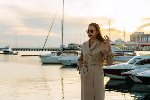 Junges schönes Mädchen mit Sonnenbrille, das bei Sonnenuntergang am Meer posiert