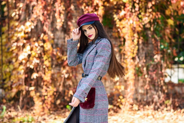 Junges schönes Mädchen mit tragendem Wintermantel und Kappe des sehr langen Haares im Herbstlaub