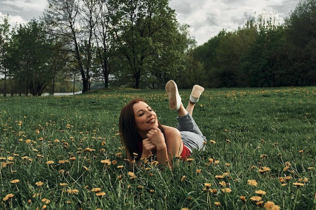 Foto junges schönes mädchen ruht im park auf dem gras mit löwenzahn. sommer hintergrund