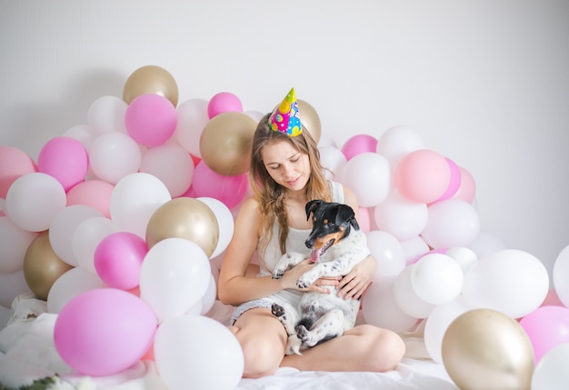 Junges schönes Mädchen wachte umgeben von Luftballons am Geburtstag mit ihrem Haustierhund auf