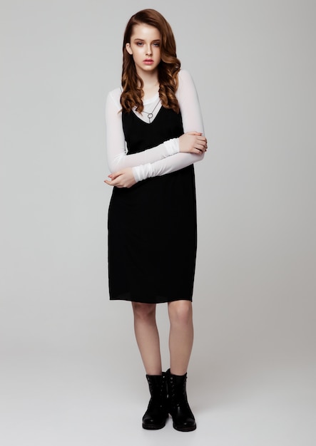 Junges schönes Mode-Modell, das schwarzes Kleid mit weißem Hemd auf Grau trägt