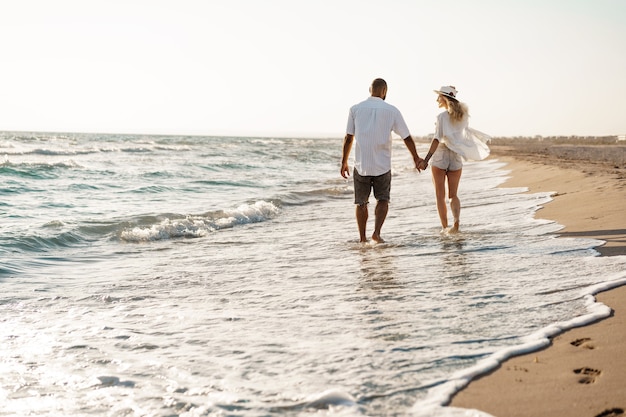 Junges schönes Paar, das am Strand nahe Meer geht