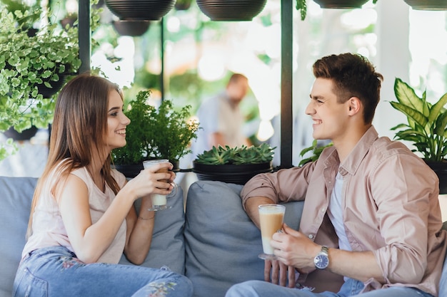 Junges schönes Paar, das auf der Sommerterrasse des Cafés spricht und Kaffee trinkt