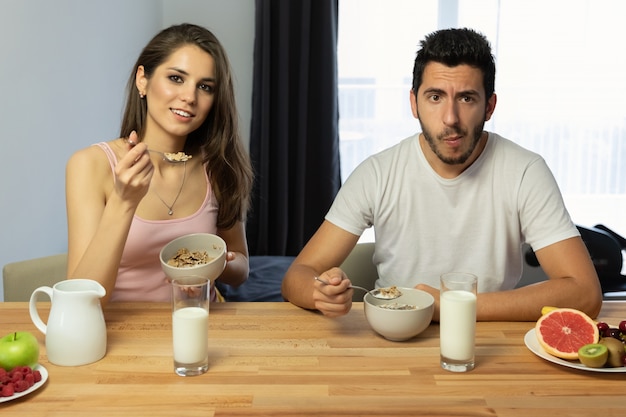 Junges schönes Paar isst Frühstücksflocken mit Beeren und Milch.