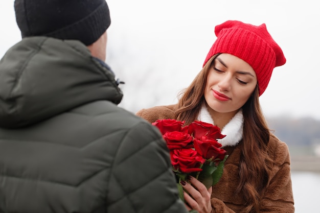 Junges schönes Paar mit roten Rosen im Freien