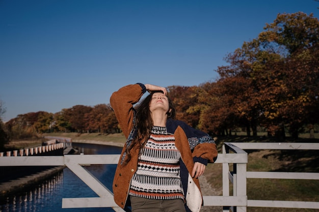 Junges schönes positives Mädchen mit langen Haaren in der Nähe des Flusses an einem sonnigen Tag.