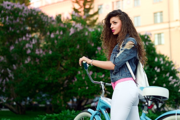 Junges schönes sexy Mädchen mit lockigem Haar und einem schönen Lächeln ruht im Park auf einem Fahrrad im Sommer