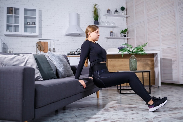 Junges schönes Sportmädchen in Leggings und einem Oberteil macht Übungen zu Hause auf der Couch. Gesunder Lebensstil. Die Frau treibt zu Hause Sport.